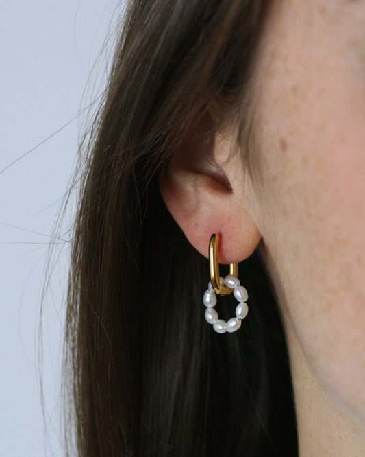 Gold hoop earring with freshwater pearl beads worn by a person against a neutral background