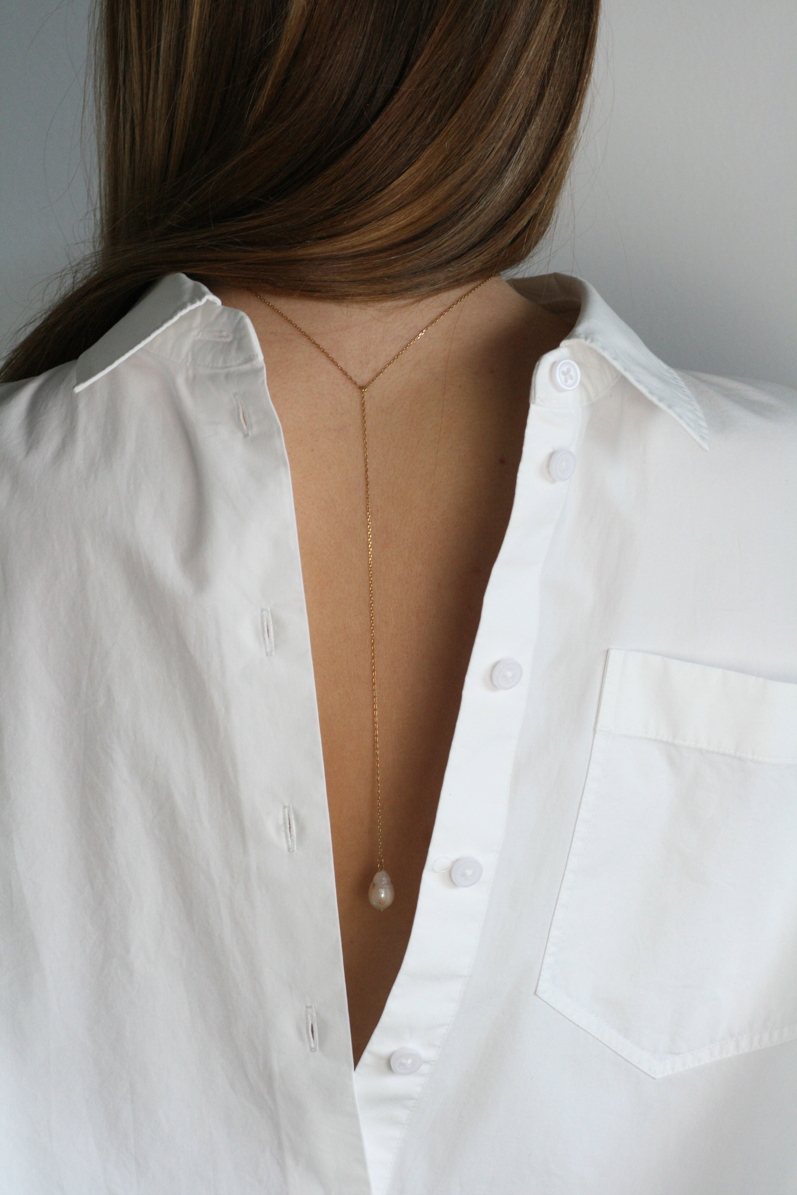 A woman's back with a y-shaped minimalistic, modern freshwater pearl VELA CHAIN necklace.