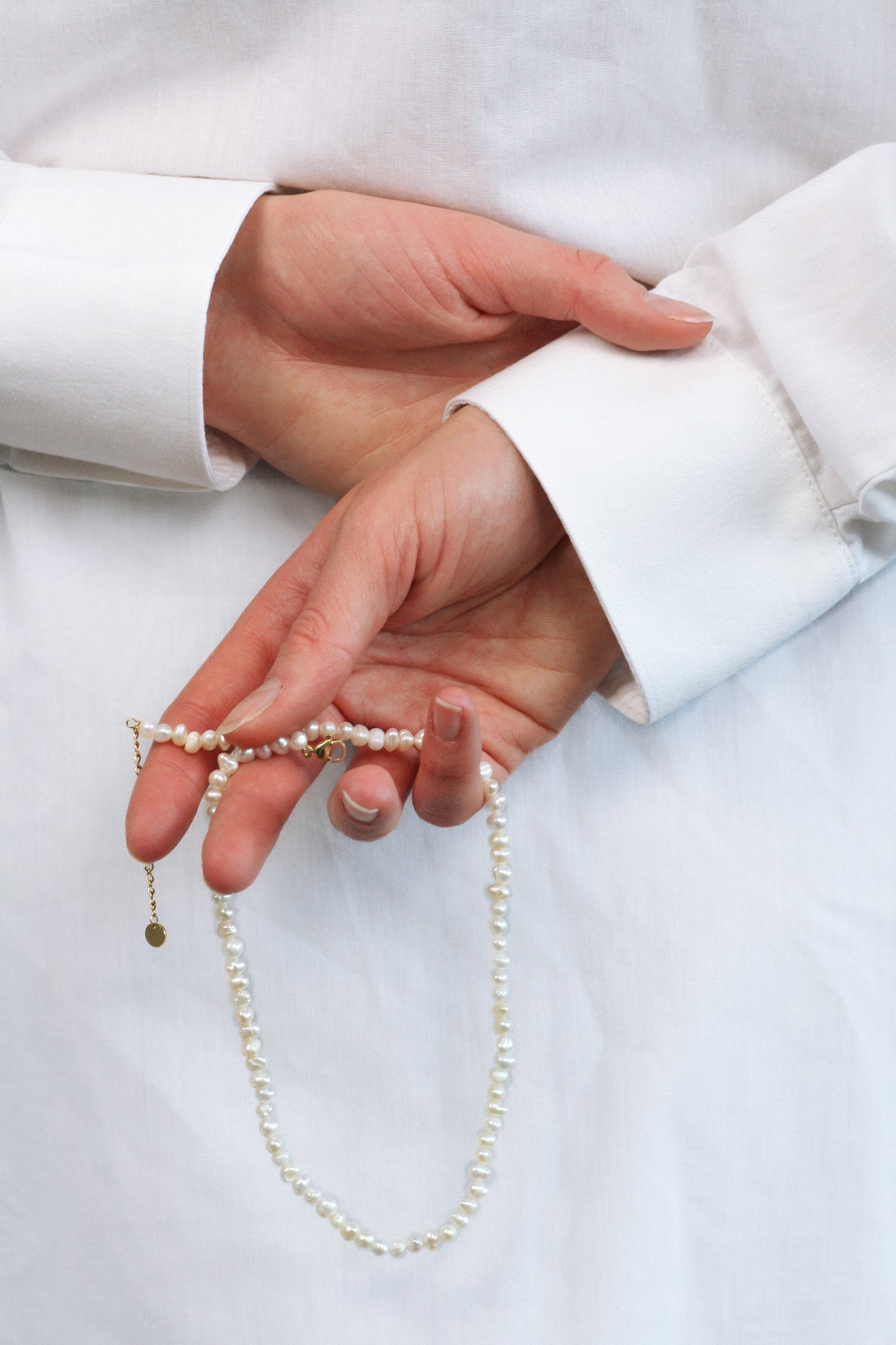 Fashion editorial photo of a woman's hands holding a pearl PULSE CHOKER necklace.