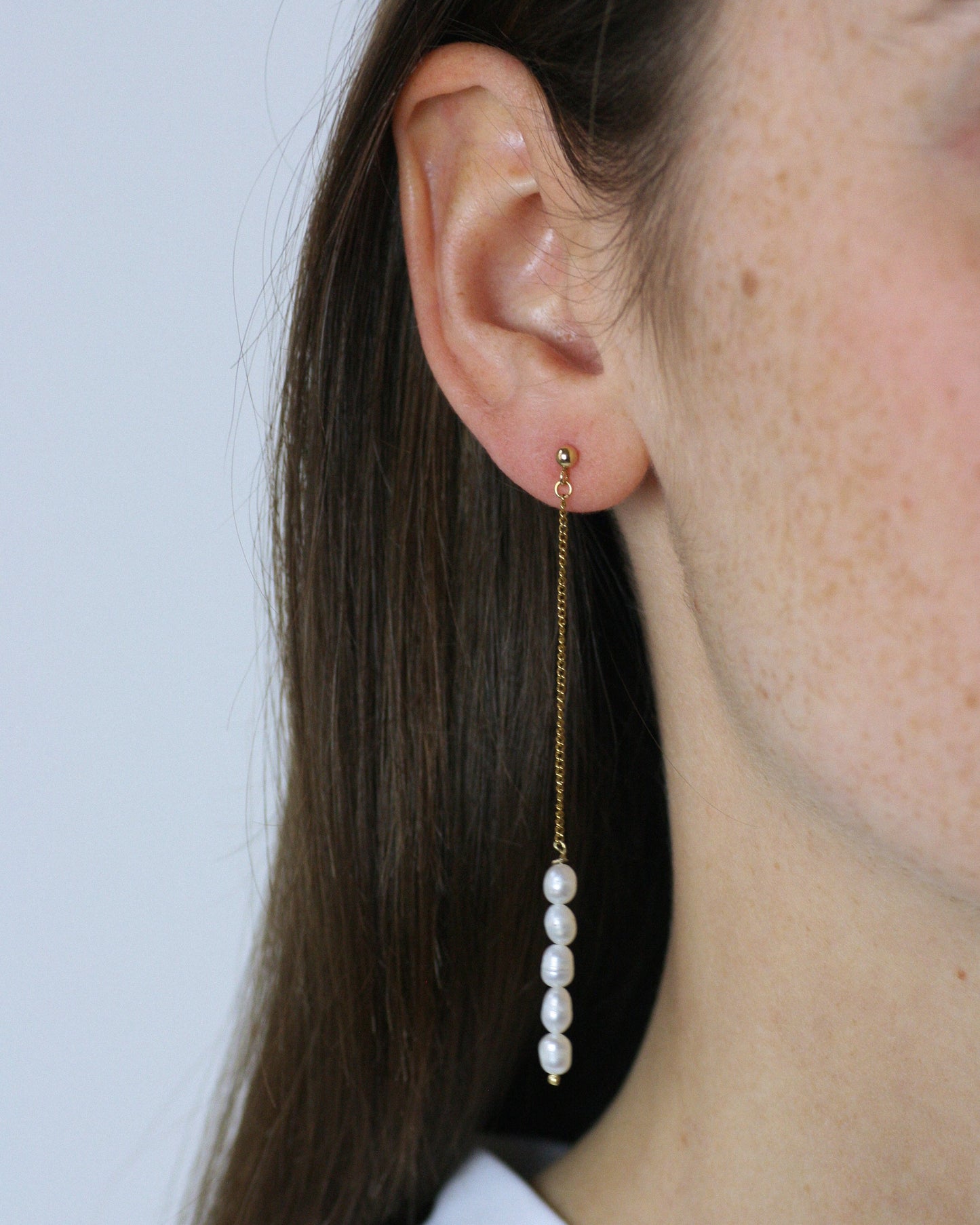 Close-up of a person wearing a gold earring with freshwater pearl drops against a light background