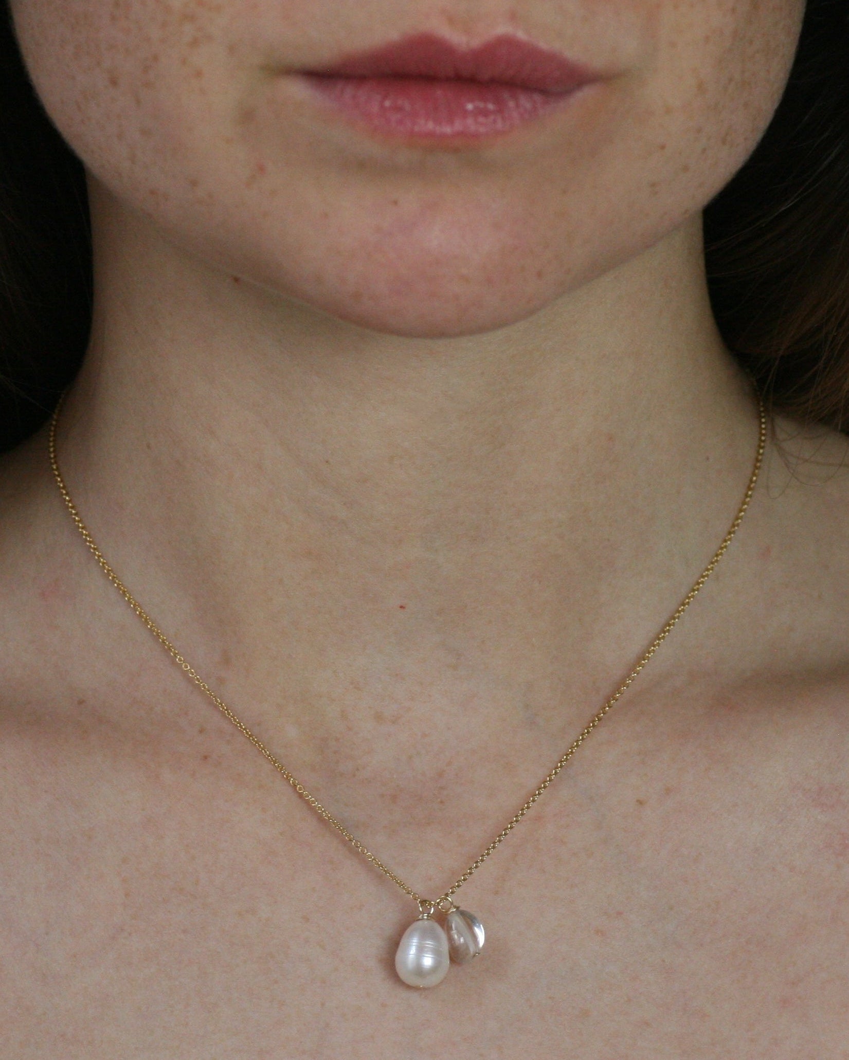 Close-up of a person wearing a gold necklace with pearl and rock crystal pendants.

